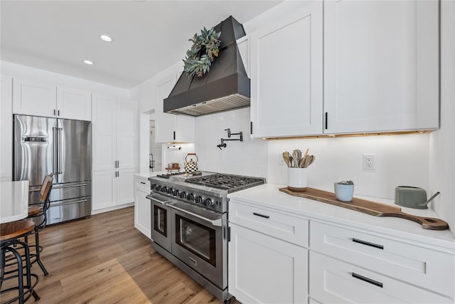 kitchen featuring white cabinetry, custom exhaust hood, high end appliances, and light wood finished floors