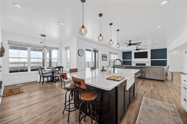 kitchen with light wood finished floors, an island with sink, light countertops, a fireplace, and a sink