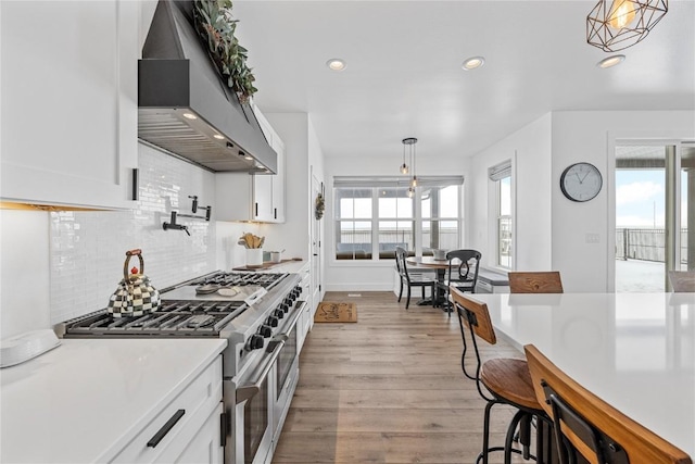 kitchen featuring white cabinets, wall chimney exhaust hood, double oven range, and light wood-style floors