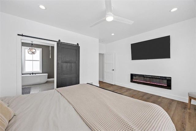 bedroom with recessed lighting, a barn door, wood finished floors, and a glass covered fireplace