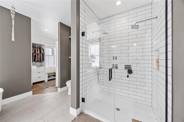 full bathroom with toilet, a shower stall, baseboards, a spacious closet, and wood tiled floor