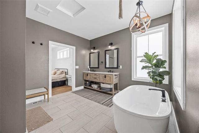 ensuite bathroom with baseboards, wood finish floors, a freestanding bath, double vanity, and ensuite bathroom