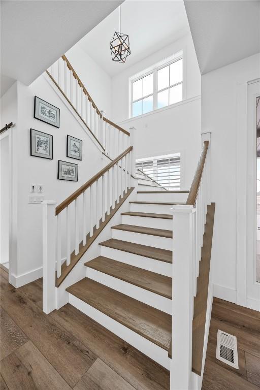 staircase featuring visible vents, baseboards, a notable chandelier, and wood finished floors