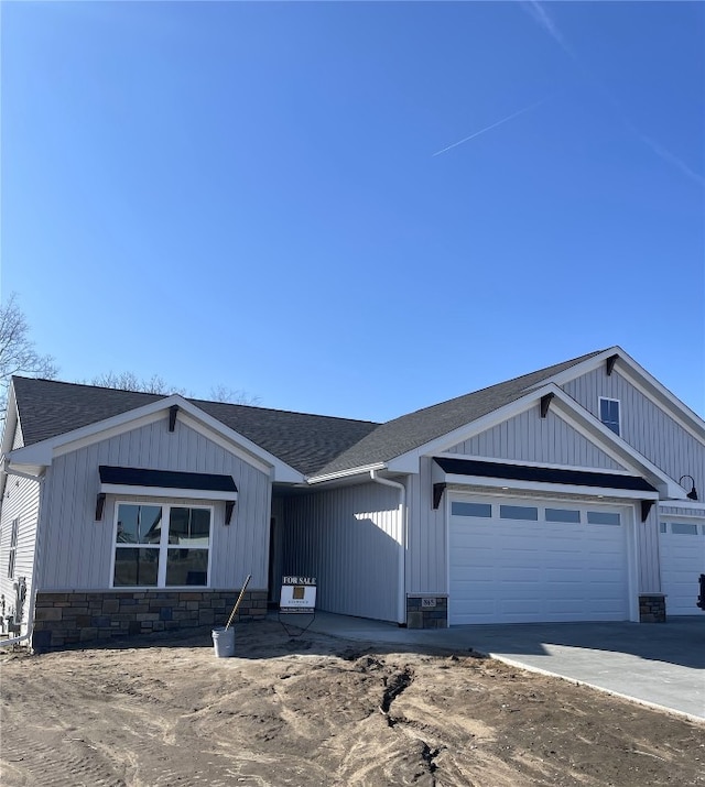 view of front facade featuring concrete driveway, a garage, stone siding, and roof with shingles