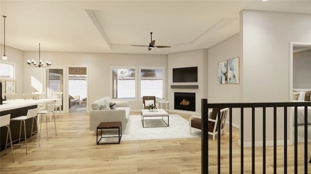 living area with a tray ceiling, light wood-style floors, a fireplace, and ceiling fan with notable chandelier