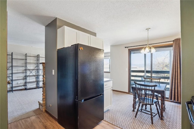 kitchen with white cabinetry, light wood-style flooring, freestanding refrigerator, a notable chandelier, and a textured ceiling