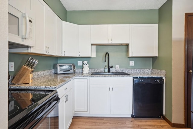 kitchen featuring black appliances, white cabinets, light stone counters, and a sink