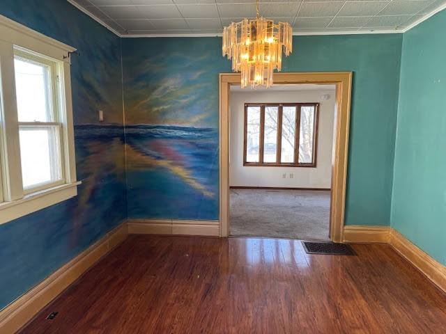 empty room with plenty of natural light, baseboards, an inviting chandelier, and wood finished floors