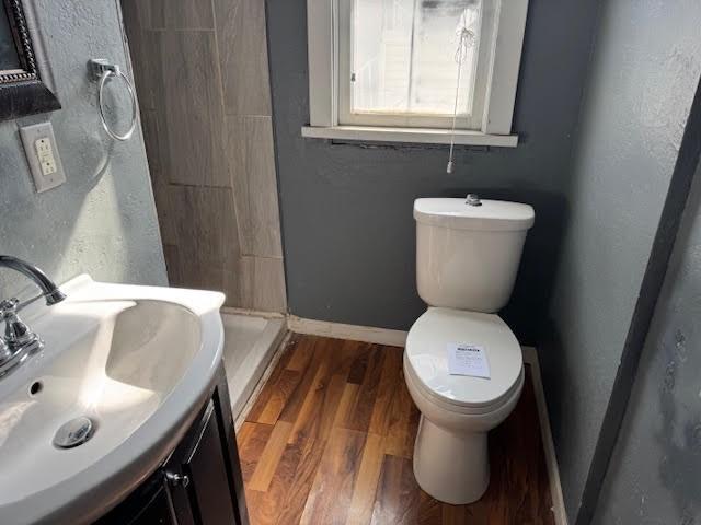 bathroom featuring vanity, wood finished floors, baseboards, a shower stall, and toilet