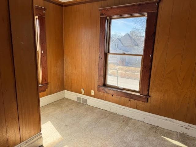 spare room with visible vents, wood walls, baseboards, and carpet