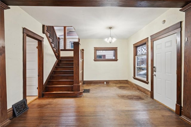 foyer with hardwood / wood-style floors, stairway, baseboards, visible vents, and a chandelier