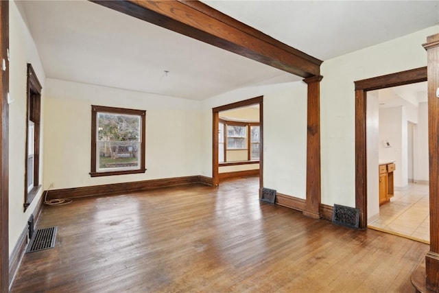 spare room with visible vents, beam ceiling, baseboards, and wood finished floors