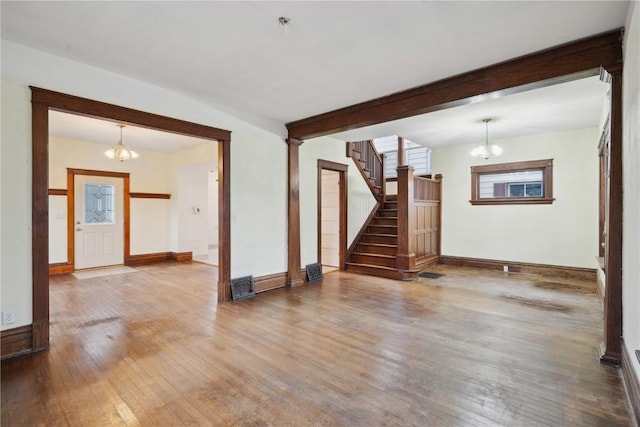 unfurnished living room with stairway, wood-type flooring, an inviting chandelier, and beam ceiling