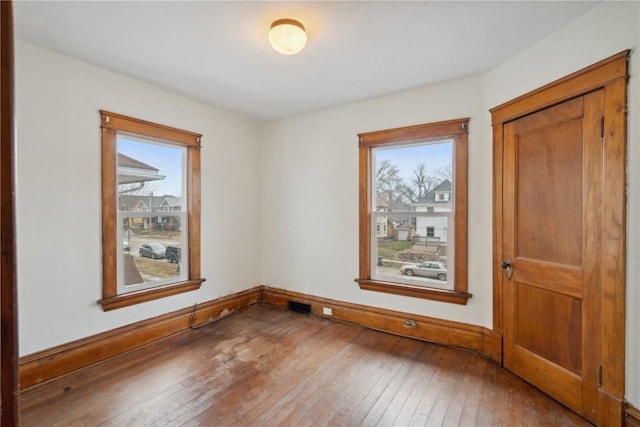 empty room with hardwood / wood-style floors, visible vents, and baseboards