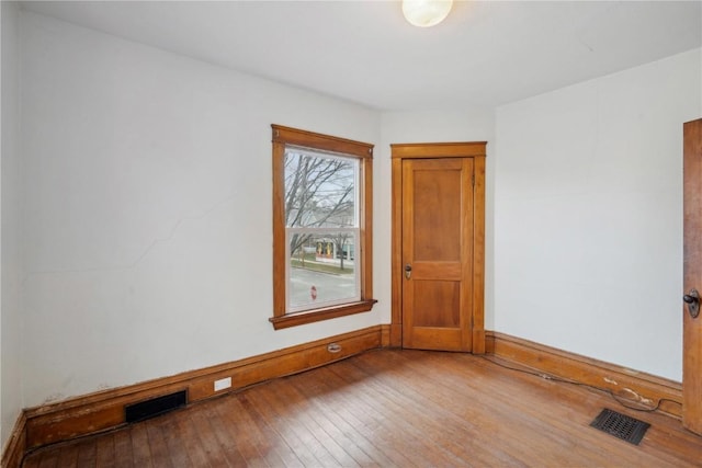 unfurnished room with visible vents, baseboards, and hardwood / wood-style floors