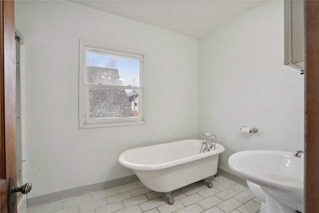 bathroom featuring tile patterned floors, a soaking tub, baseboards, and a sink