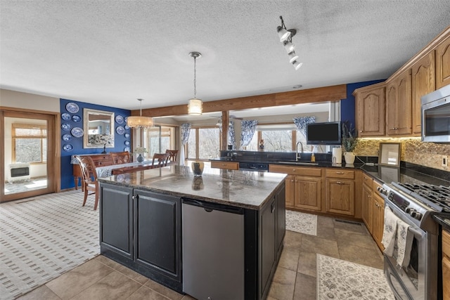 kitchen featuring tasteful backsplash, a kitchen island, decorative light fixtures, stainless steel appliances, and a sink