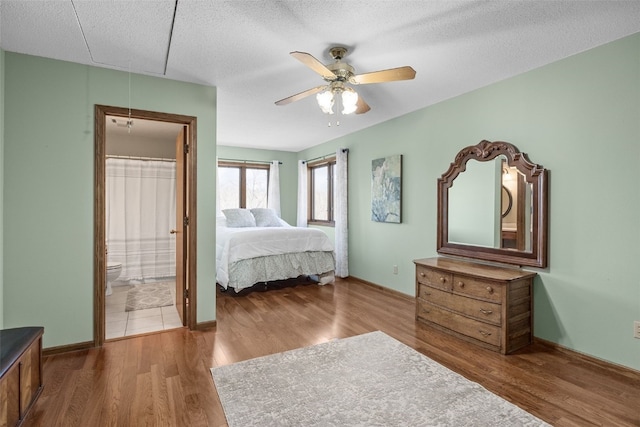 bedroom featuring baseboards, attic access, ensuite bathroom, wood finished floors, and a textured ceiling