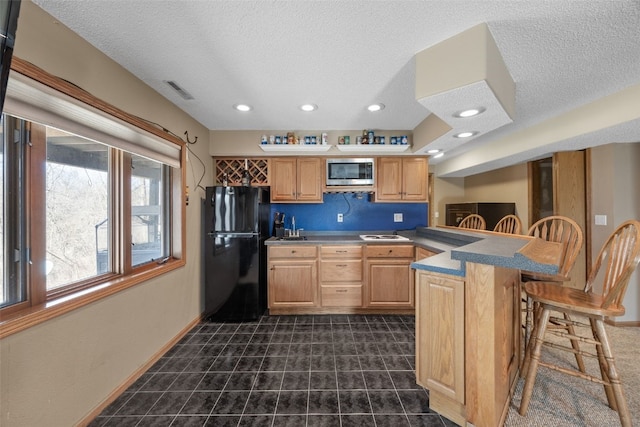 kitchen featuring a breakfast bar, a peninsula, freestanding refrigerator, light brown cabinetry, and stainless steel microwave