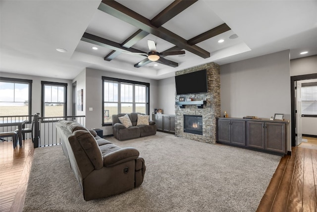 living area featuring coffered ceiling, beam ceiling, recessed lighting, a stone fireplace, and hardwood / wood-style flooring