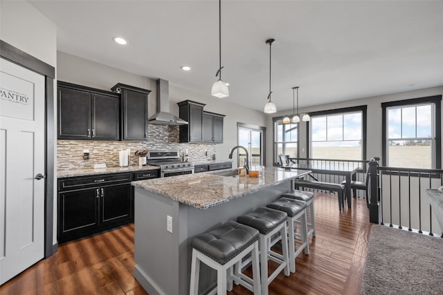 kitchen with stainless steel gas range oven, a kitchen bar, a sink, wall chimney range hood, and decorative backsplash