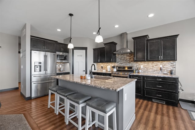 kitchen featuring a sink, backsplash, dark cabinetry, stainless steel appliances, and wall chimney range hood