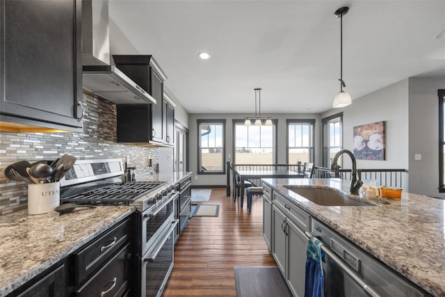 kitchen with dark wood-style floors, a sink, decorative backsplash, stainless steel appliances, and wall chimney exhaust hood