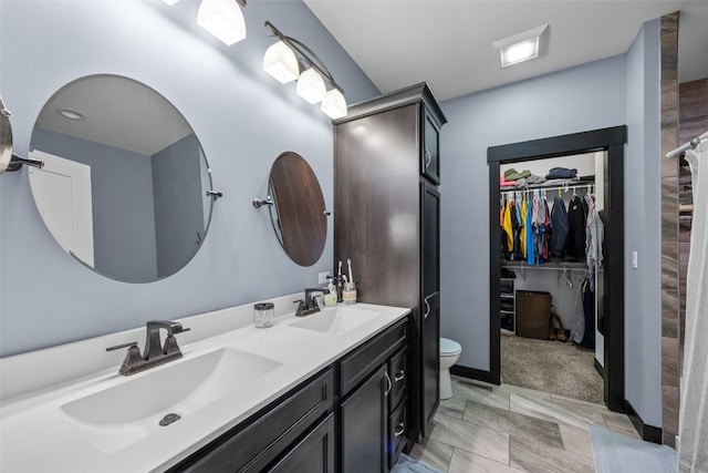 full bath featuring double vanity, a spacious closet, toilet, and a sink