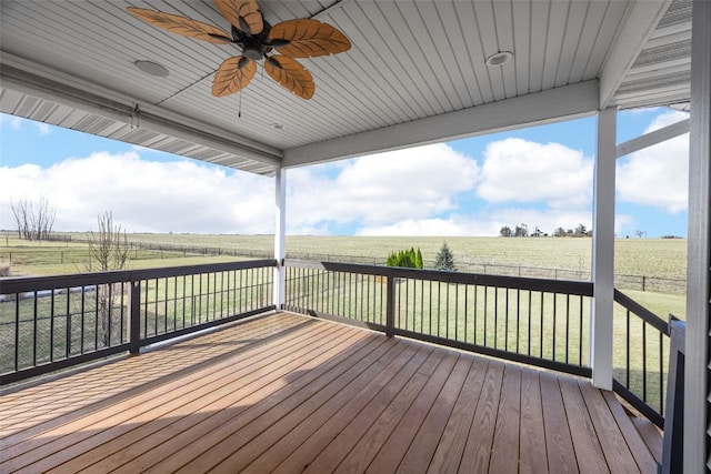 wooden deck featuring a rural view, ceiling fan, a lawn, and fence