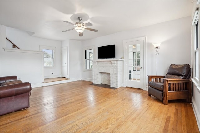 living room with baseboards, a brick fireplace, ceiling fan, and light wood finished floors