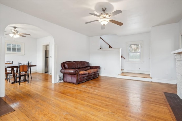 living room featuring ceiling fan, baseboards, stairs, light wood-style floors, and arched walkways