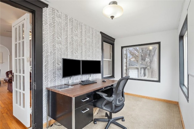 home office with baseboards, arched walkways, wood finished floors, and an accent wall