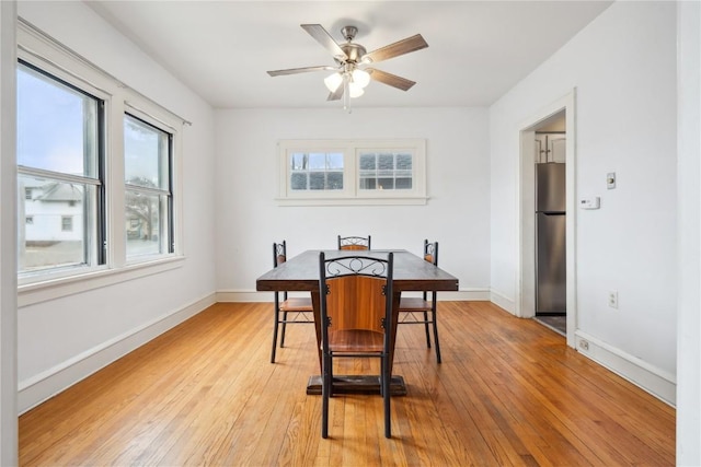 dining room featuring light wood-style flooring, a ceiling fan, and baseboards