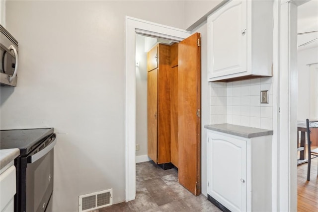 kitchen with visible vents, electric stove, stainless steel microwave, backsplash, and white cabinets