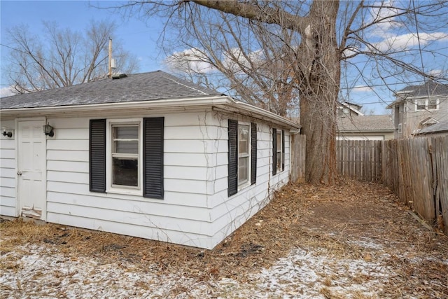 view of side of property with roof with shingles and fence