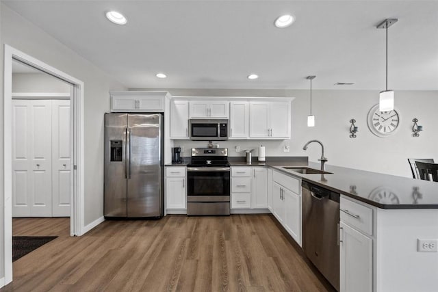 kitchen with dark countertops, a peninsula, wood finished floors, stainless steel appliances, and a sink