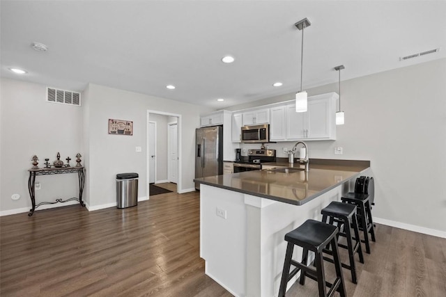 kitchen featuring a kitchen bar, visible vents, a sink, dark wood finished floors, and stainless steel appliances