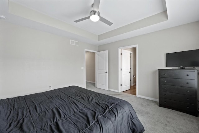 carpeted bedroom with a raised ceiling, baseboards, visible vents, and ceiling fan