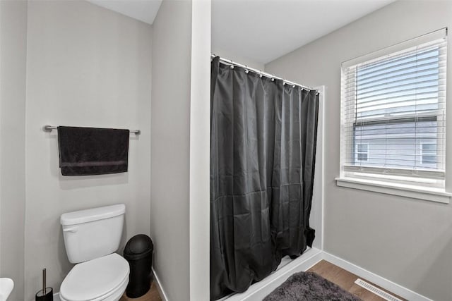 bathroom featuring curtained shower, toilet, wood finished floors, and baseboards