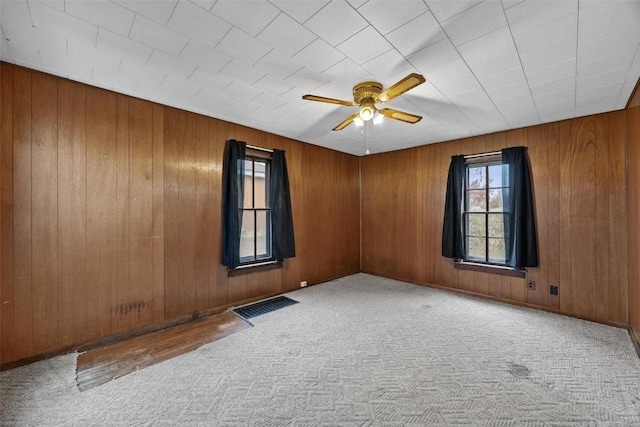 carpeted empty room with visible vents, wooden walls, and a ceiling fan