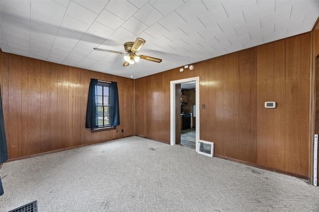 carpeted spare room with wooden walls, visible vents, and ceiling fan