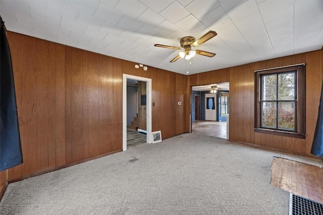 carpeted spare room featuring stairs, wooden walls, visible vents, and ceiling fan