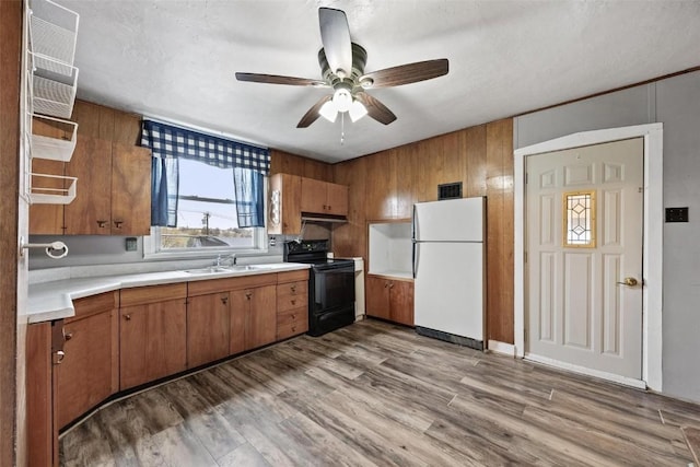 kitchen with brown cabinets, a sink, freestanding refrigerator, black / electric stove, and light countertops