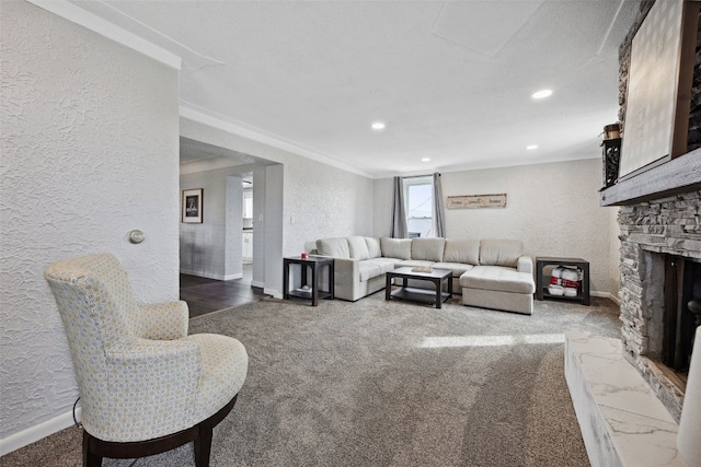 carpeted living area with baseboards, recessed lighting, a stone fireplace, crown molding, and a textured wall