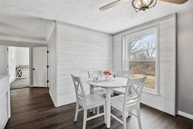 dining space with wooden walls, ceiling fan, baseboards, dark wood-style floors, and a textured ceiling