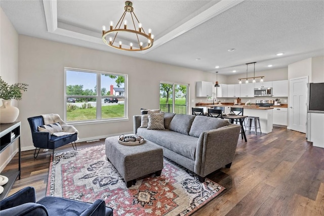 living room featuring dark wood finished floors, a chandelier, baseboards, and a tray ceiling