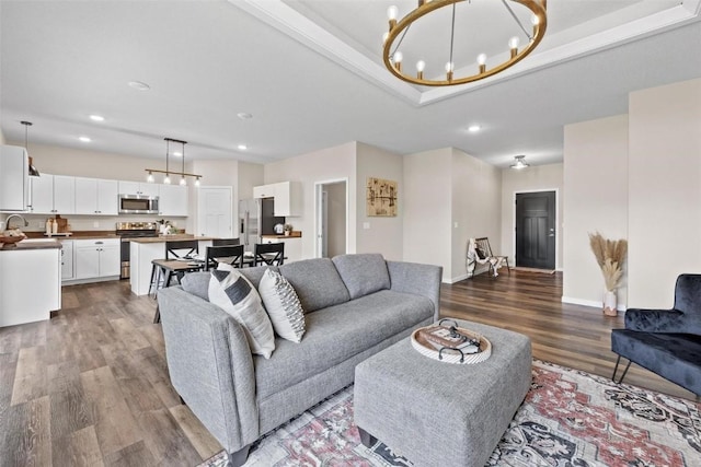 living area featuring a notable chandelier, a tray ceiling, wood finished floors, recessed lighting, and baseboards