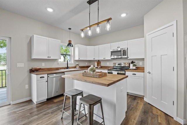 kitchen with butcher block countertops, appliances with stainless steel finishes, white cabinetry, and a kitchen bar