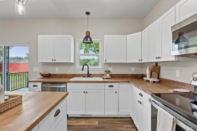 kitchen featuring butcher block countertops, stainless steel appliances, hanging light fixtures, white cabinetry, and a sink