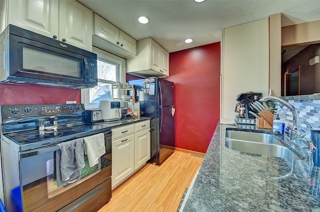 kitchen with light wood-type flooring, black appliances, a sink, dark stone countertops, and white cabinets